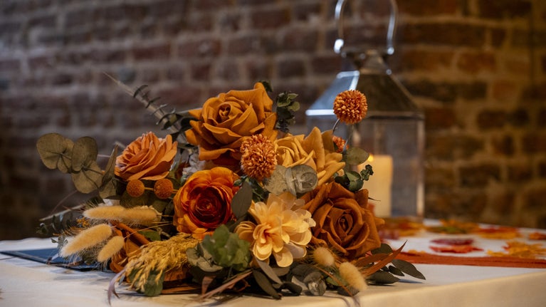 Autumnal wedding floral arrangement featuring orange and cream flowers, foliage and dried grasses displayed on a ceremony table inside the historic Great Tower at Tattershall Castle. Lincolnshire wedding venue.